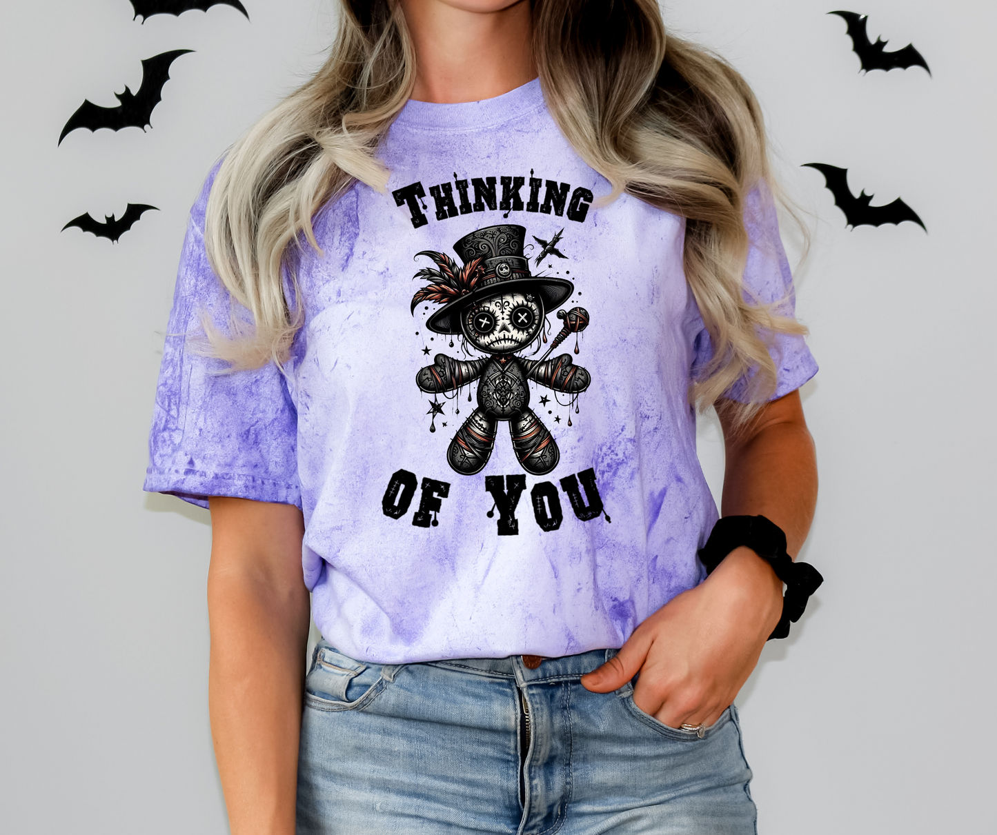 A purple tie-dye shirt with a graphic design of a Voodoo Doll with 'Thinking of You' text.