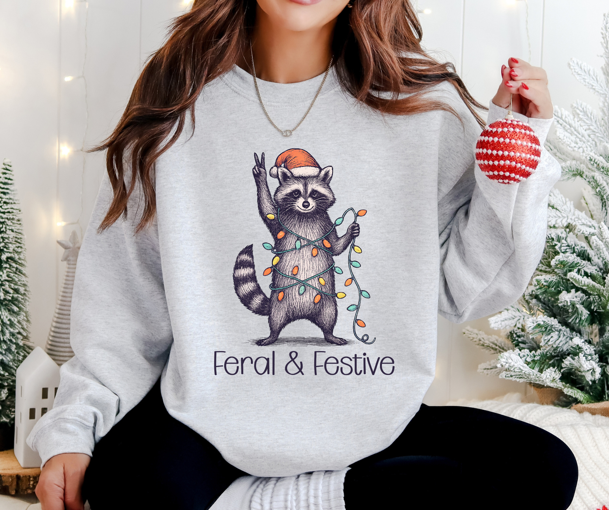 Holiday Sweatshirt With A Festive Raccoon Wrapped in Lights with A Santa Hat And The Text Feral & Festive