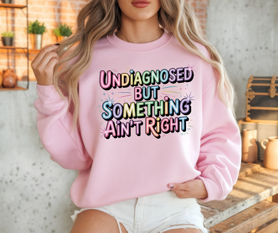 Pink Crewneck Shirt With A Graphic Text "Undiagnosed But Something Ain't Right"