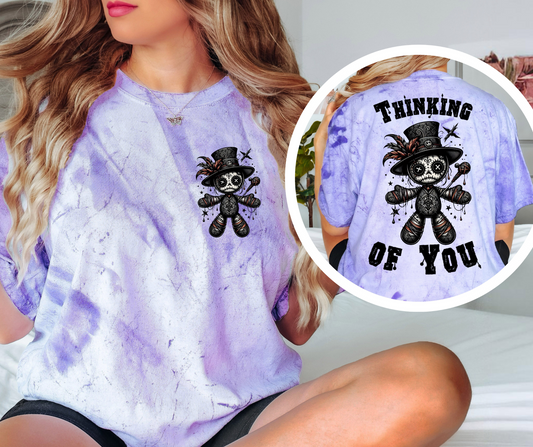  A purple tie-dye shirt with a graphic design of a Voodoo Doll with 'Thinking of You' text.